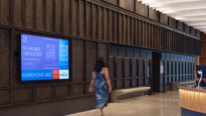 XYZ-Technologies_SANAAQ_A young-woman-walks-past-a-large-digital-screen-reception-area