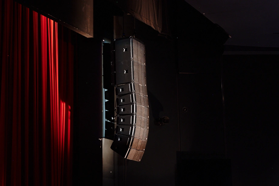 Système line array professionnel en salle de spectacle assurant une couverture sonore uniforme avec haut-parleurs suspendus et caissons de basse