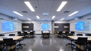 Salle de classe équipée de projecteurs multiples avec bureaux longeants les murs de la salle